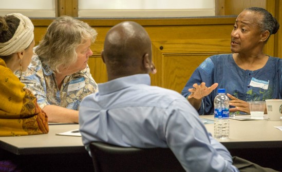 Photo of an African American woman speaking to three individuals at a table